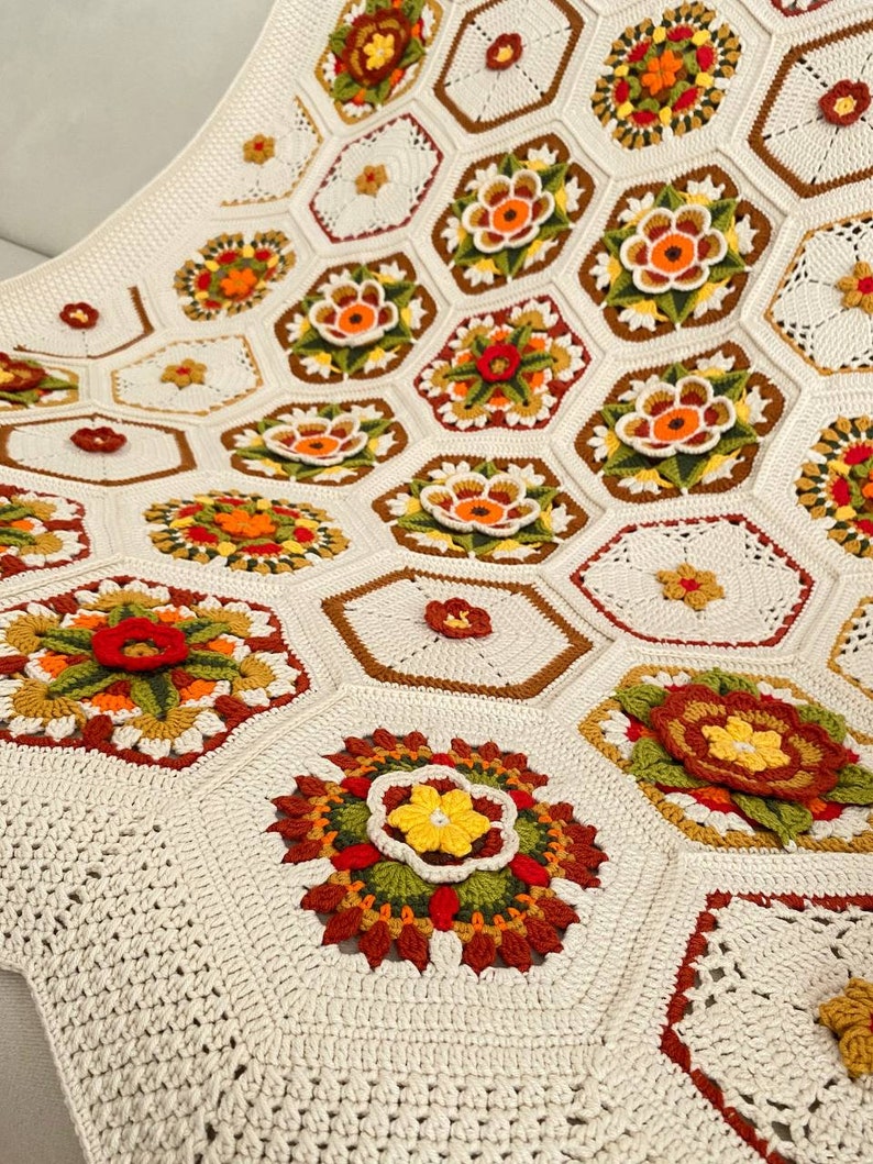 May include: A crocheted blanket with a white background and colorful floral motifs. The blanket is made up of hexagonal shapes with intricate designs in shades of orange, yellow, green, and red.