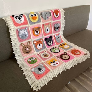 Puede incluir: Una manta de beb&eacute; de crochet en color rosa y blanco. La manta presenta una variedad de caras de animales, incluyendo un panda, un pato, un elefante, un zorro, una cebra, un oso, un perro, un rat&oacute;n, un tigre, una rana, un koala y un mono.
