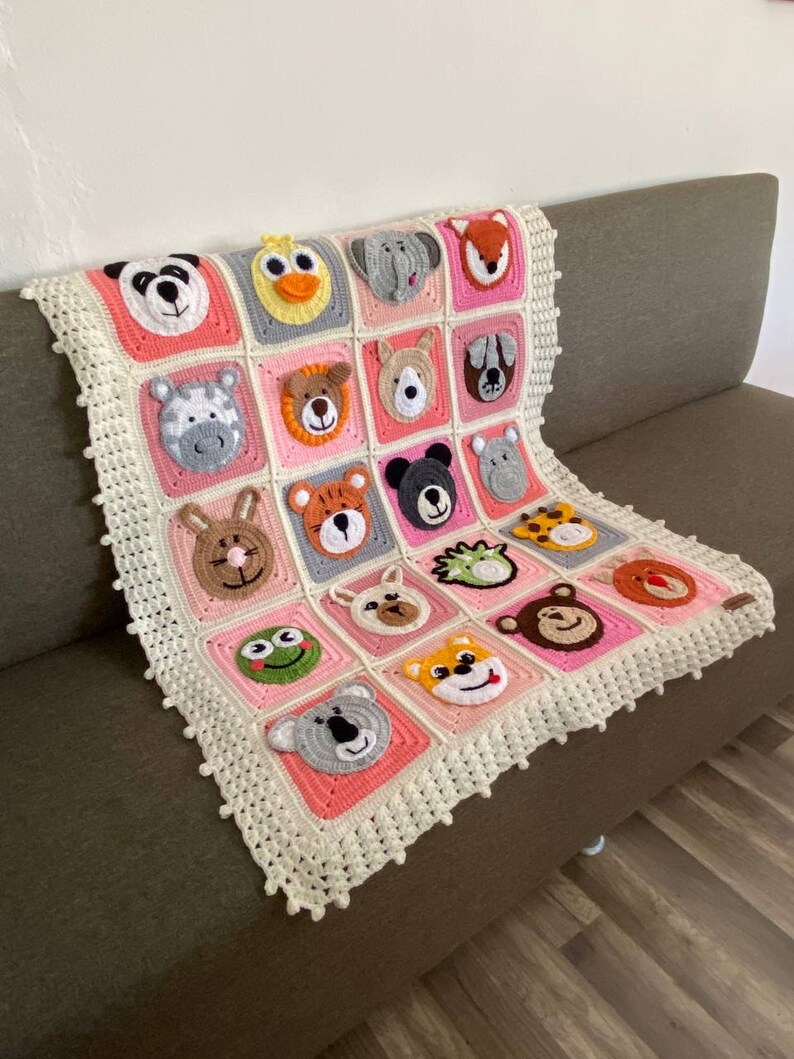 Puede incluir: Una manta de beb&eacute; de crochet en color rosa y blanco. La manta presenta una variedad de caras de animales, incluyendo un panda, un pato, un elefante, un zorro, una cebra, un oso, un perro, un rat&oacute;n, un tigre, una rana, un koala y un mono.