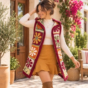 May include: A sleeveless hooded vest crafted from multicolored crochet granny squares featuring floral patterns in shades of burgundy, orange, yellow, and cream, with a ribbed burgundy border along the front opening and hood edges.