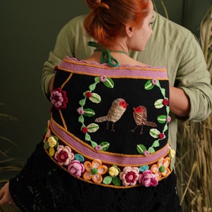 May include: A black crochet shawl with a floral design and two embroidered birds. The shawl has a pink and yellow border with a scalloped edge.