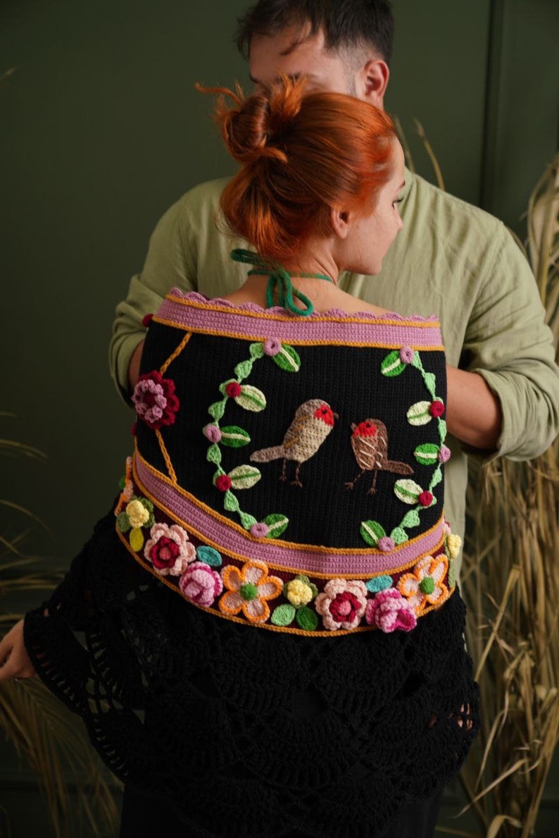 May include: A black crochet shawl with a floral design and two embroidered birds. The shawl has a pink and yellow border with a scalloped edge.