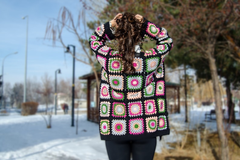May include: A black crochet cardigan with a colorful geometric pattern. The cardigan features squares with pink, green, and white accents.