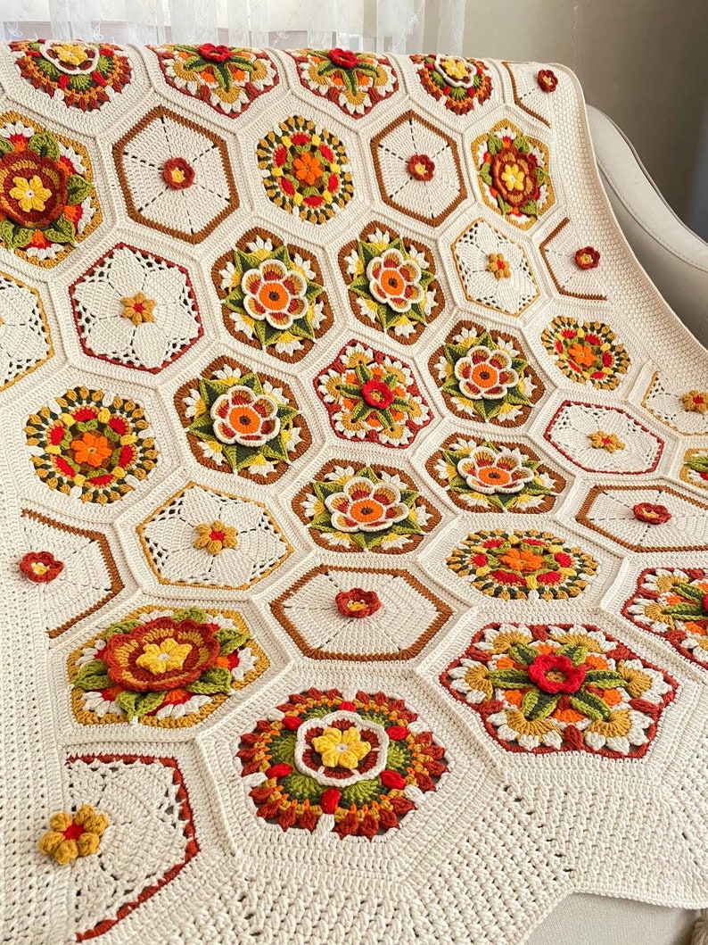 May include: A crocheted blanket with a hexagonal pattern featuring a variety of colorful flowers in shades of red, orange, yellow, green, and brown. The blanket is made with a white yarn and has a delicate, lacy texture.