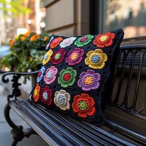 Peut inclure: Un coussin noir avec un motif de fleurs crochetées colorées. Le coussin est posé sur un banc en métal noir.