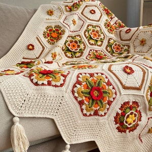 May include: A crocheted throw blanket with a white background and colorful floral patterns. The blanket has a fringe border and is draped over a couch.