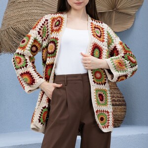 Pu&ograve; includere: Un cardigan all'uncinetto con un motivo geometrico in tonalit&agrave; di rosso, arancione, verde e beige. Il cardigan ha una vestibilit&agrave; rilassata e una lunghezza lunga.