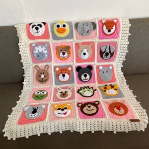Puede incluir: Una manta de beb&eacute; de crochet con un borde blanco y cuadrados rosas con diferentes caras de animales. La manta est&aacute; hecha con hilo suave y es perfecta para la habitaci&oacute;n de un beb&eacute;.