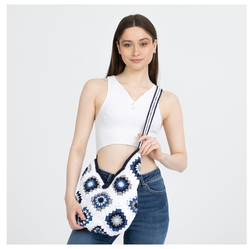 May include: A white crochet bag with a blue and white geometric pattern. The bag has a long strap and is worn over the shoulder.