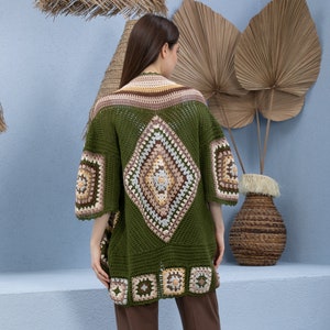 May include: A green crochet cardigan with a diamond-shaped pattern in the back and square patterns on the sleeves and bottom hem. The cardigan is made with a variety of colors, including brown, beige, and white.
