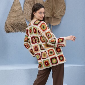Pu&ograve; includere: Un cardigan all'uncinetto con un motivo geometrico colorato in tonalit&agrave; di rosso, arancione, verde e crema. Il cardigan &egrave; aperto sul davanti e ha maniche lunghe.