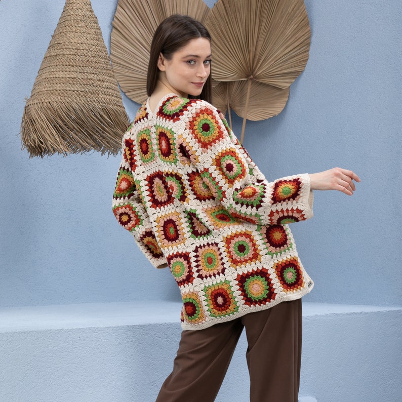 Pu&ograve; includere: Un cardigan all'uncinetto con un motivo geometrico colorato in tonalit&agrave; di rosso, arancione, verde e crema. Il cardigan &egrave; aperto sul davanti e ha maniche lunghe.