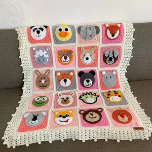 Puede incluir: Una manta de beb&eacute; de crochet con un borde rosa y blanco. La manta presenta una variedad de caras de animales, incluyendo un panda, un pato, un elefante, un zorro, una cebra, un oso, un perro, un koala, una rana, una jirafa y un mono.