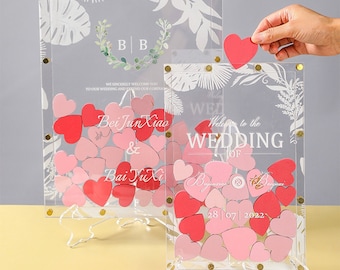May include: A clear acrylic wedding guest book with a floral design and the text "Welcome to the Wedding of Bei Jun Xiao & Bai Yu Xi 28|07|2022". Guests can leave their well wishes by placing pink and red heart-shaped cards inside the box.