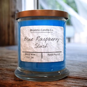 May include: A blue glass candle jar with a white label that reads "Majestic Candle Co. Blue Raspberry Slush Blend Wax 12oz. Jar Hand Poured".