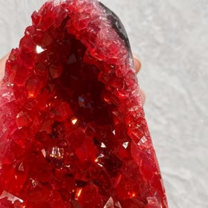 May include: A striking red crystal geode, showcasing a crystalline interior. The geode's exterior is a rich red hue, while the inside is packed with tiny, reflective crystals. The overall form is irregular and natural.