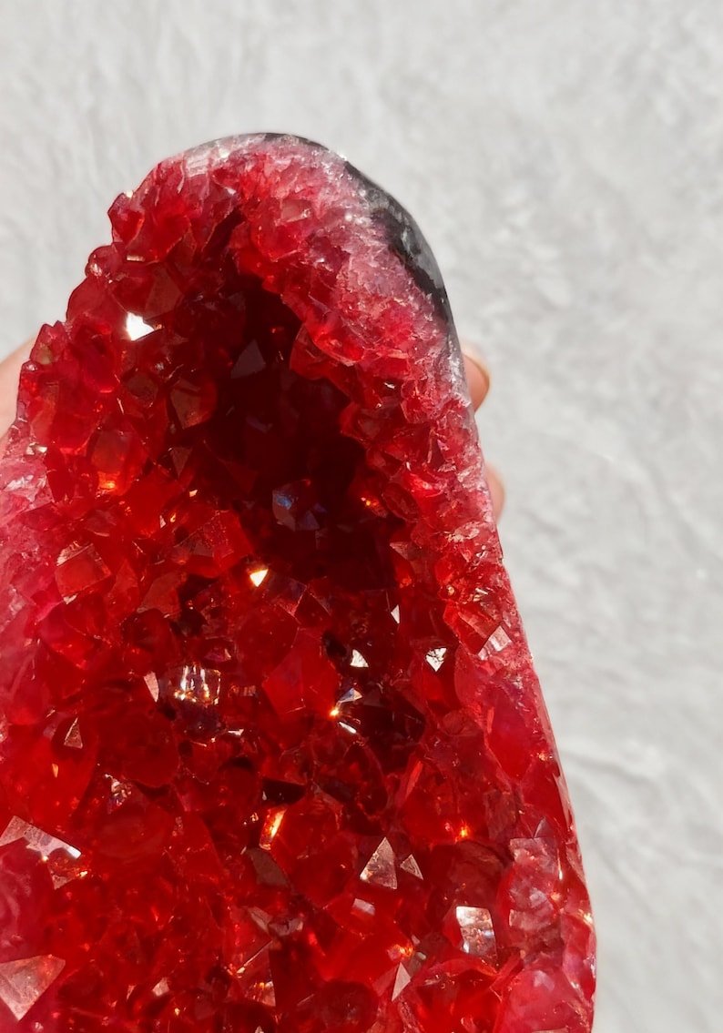 May include: A striking red crystal geode, showcasing a crystalline interior. The geode's exterior is a rich red hue, while the inside is packed with tiny, reflective crystals. The overall form is irregular and natural.