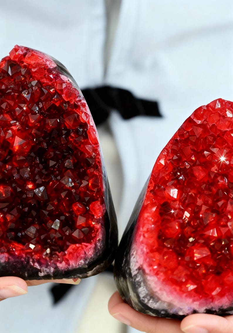 May include: Two halves of a geode with a vibrant red crystal interior. The crystals sparkle, contrasting with the dark, rough exterior. The geode is held up against a white background.