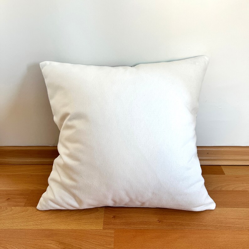 May include: A white, plain pillow with a soft, plush texture. The pillow is lying flat on a wooden floor.