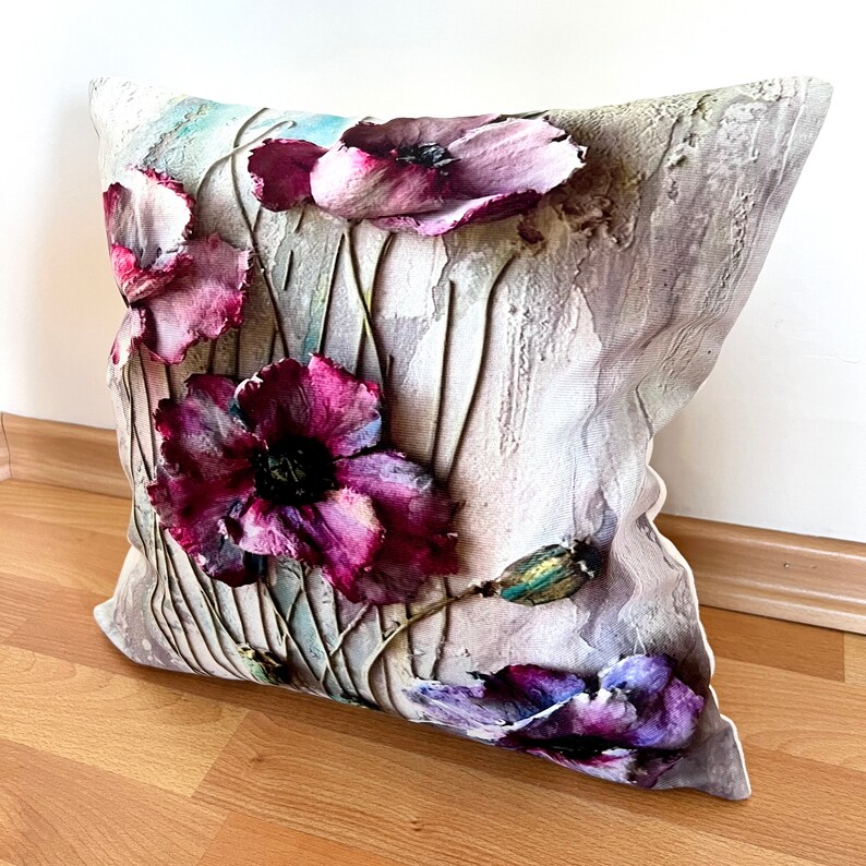 May include: A decorative pillow with a floral design featuring purple and pink poppies on a textured beige background.