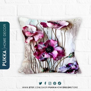 May include: A decorative pillow with a floral design featuring pink and purple poppies on a textured beige background. The pillow has a subtle distressed look and is perfect for adding a touch of nature to any room.