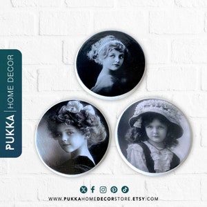 May include: Three round white ceramic wall decor plates with black and white vintage photographs of young girls. Each plate features a different image of a girl with a different hairstyle and clothing.