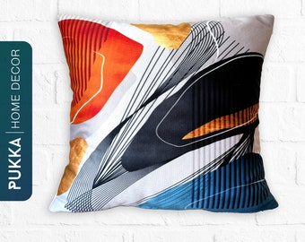 Puede incluir: Una almohada cuadrada con un diseño geométrico abstracto en negro, naranja, rojo, dorado y azul. La almohada tiene un fondo blanco.