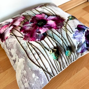 May include: A decorative pillow with a floral design featuring pink and purple poppies on a textured white background.