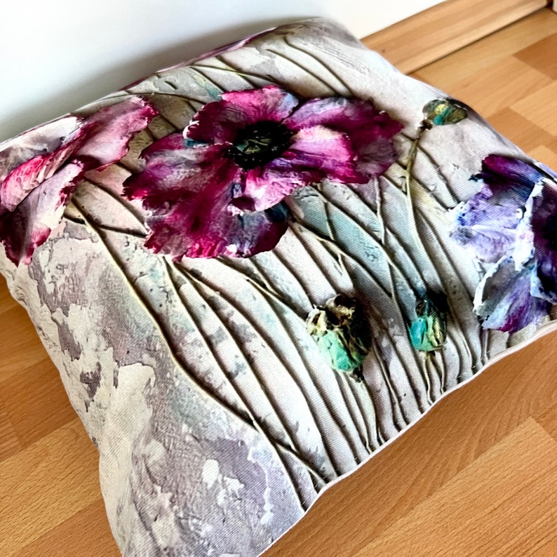 May include: A decorative pillow with a floral design featuring pink and purple poppies on a textured white background.