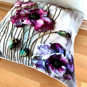 May include: A white pillow with a floral design featuring purple and pink poppies on a textured background.