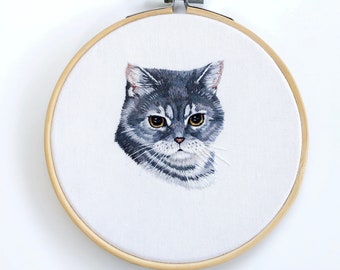 May include: Embroidered portrait of a gray cat with yellow eyes in a wooden embroidery hoop.