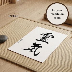 May include: A rectangular white paper print featuring black Japanese calligraphy characters for Reiki. The print is displayed on a textured tan mat. The text REIKI and for your meditaion room are visible in the image, along with a small dark stone.