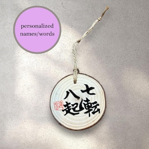 Peut inclure: Ornement rond en bois clair avec des veines apparentes. Il présente une calligraphie japonaise noire et un tampon rouge. Un cercle violet clair avec le texte "personalized names/words" est en haut à gauche. L'ornement est suspendu par une ficelle naturelle.