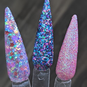 Puede incluir: Tres muestras de uñas con purpurina. La primera presenta purpurina morada, roja y azul con formas de estrella. La segunda es una mezcla de purpurina azul y morada. La tercera es purpurina rosa sólida. Todas están en palitos de plástico transparente.