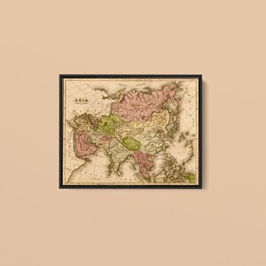 May include: A framed vintage map of Asia featuring a beige background with landmasses highlighted in muted pink and green tones. The map displays detailed geographical lines, labels, and the word ASIA printed in the upper left corner area.