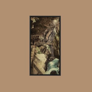 May include: A framed vertical wall art print depicting a narrow gorge with towering dark rock walls and a wooden walkway built along the side. A rushing turquoise river flows through the bottom of the canyon, with light filtering from above.