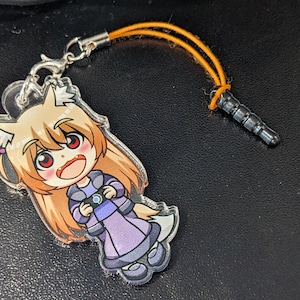 Puede incluir: Un llavero de acrílico transparente con un personaje de dibujos animados con cabello largo y rubio, ojos rojos y un vestido morado. El personaje sostiene un objeto azul en sus manos. El llavero está unido a un cordón negro y naranja.