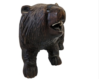 May include: A hand-carved wooden bear figurine with a detailed, realistic design. The bear is standing on all fours with its mouth open, revealing a set of teeth. The figurine is painted in a dark brown color.