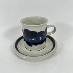 May include: A white ceramic coffee cup and saucer with a blue floral design. The cup has a handle and the saucer has a blue rim.
