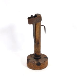 May include: A vintage wooden candle holder with a metal hook and a small metal piece at the top. The candle holder has a round wooden base and a cylindrical wooden body. The metal components are a rusty brown colour.
