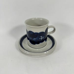 May include: A white ceramic coffee cup and saucer with a blue floral design. The cup has a handle and the saucer has a rim.