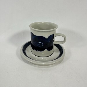 May include: A white ceramic coffee cup with a blue floral design and a matching saucer. The cup has a handle and the saucer has a blue rim.