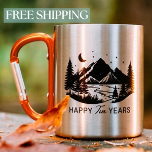 May include: A stainless steel camping mug with a black mountain scene and the text "HAPPY Ten YEARS". The mug has an orange carabiner handle.