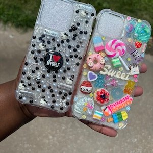 May include: Two clear phone cases decorated with colorful embellishments. One case features black and white polka dots, a heart with the text "I love myself", and the words "Fearless", "Brave", and "Willpower". The other case features a variety of colorful candies, donuts, and the text "Sweet" and "Dunkin' Donuts".