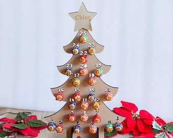 May include: A wooden Christmas tree advent calendar with the name Chloe at the top. The tree is decorated with 25 numbered circles, each with a lollipop inside. The lollipops are various colors and flavors. The tree is standing on a table with red poinsettia flowers.