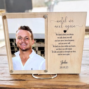 May include: A wooden photo frame with a picture of a man and a message that reads "until we meet again". The message continues with a poem about remembering a loved one. The frame has a stand and is made of light wood.