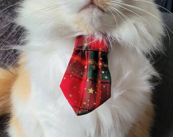 May include: A white and orange cat wearing a red and green plaid bow tie with gold stars. The cat is sitting on a gray couch.