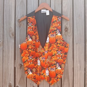 May include: A sleeveless vest featuring a vibrant Halloween-themed print with orange pumpkins, small teddy bears, and white ghosts on a black background. The garment has a V-neckline, a button-front closure, and a solid black interior lining with a label.