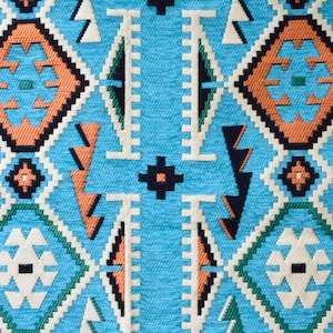 May include: A close-up of a blue fabric with a geometric pattern in shades of orange, white, and black. The pattern is reminiscent of traditional Native American designs.