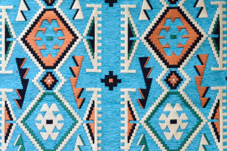 May include: A close-up of a blue fabric with a geometric pattern in shades of orange, white, and black. The pattern is reminiscent of traditional Native American designs.